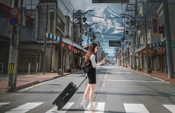 Woman is dragging luggage on a road in Fujiyoshida with the background of Mount Fuji, Japan