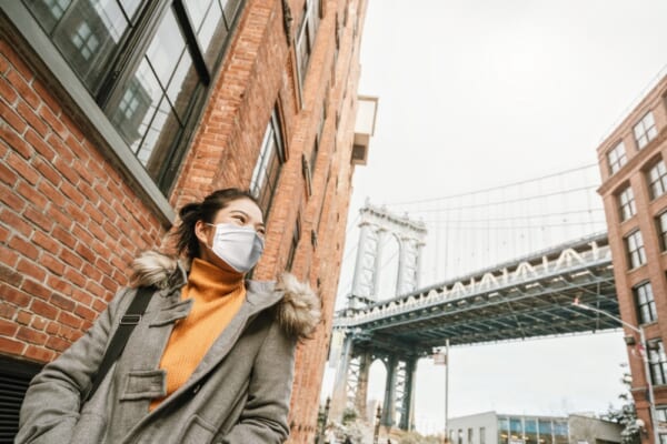 asian attractive Woman traveller wearing a face pollution mask to protect herself from the coronavirus with background of Down Under the Manhattan Bridge Overpass near the Manhattan Bridge Newyork US