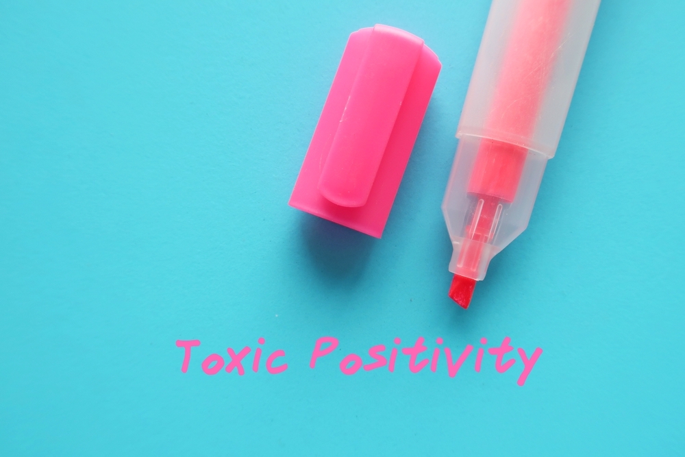 Pink highlight pen text on blue background - TOXIC POSITIVITY means being an optimist and engaging in positive thinking, rejects difficult emotions - takes positive thinking to overgeneralized extreme