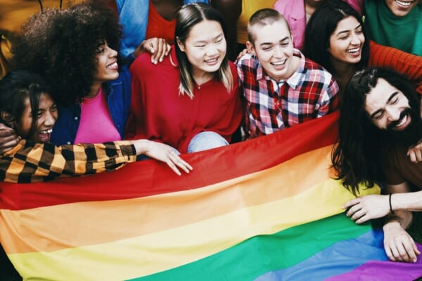 Diverse people having fun holding LGBT rainbow flag outdoor - Multiracial friends having fun together after gay pride event - Focus on center bald girl face